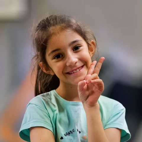 meisje kijkt blij in de camera en vormt met haar hand het 'V' teken