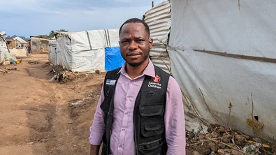 Gabriel staat in een vluchtelingenkamp in de DRC. Hij draagt een zwart Save the Children hesje.