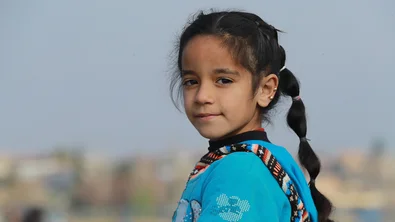 De achtjarige Amal kijkt in de camera, terwijl ze in een vluchtelingenkamp in Syrië staat