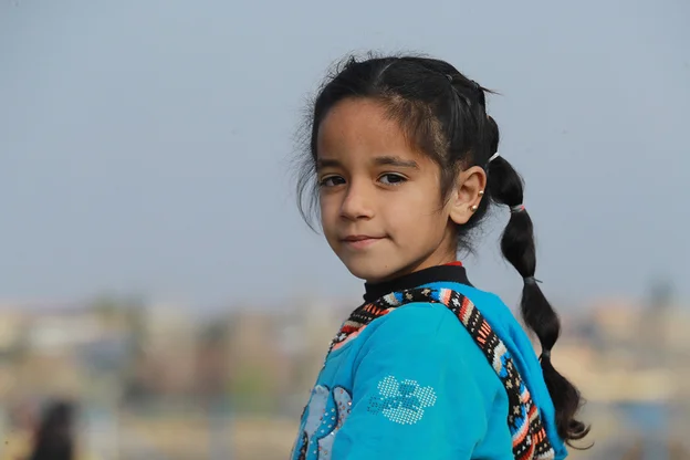 De achtjarige Amal kijkt in de camera, terwijl ze in een vluchtelingenkamp in Syrië staat