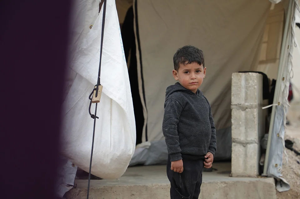 Een kleine jongen staat voor zijn tent in een Syrisch vluchtelingenkamp