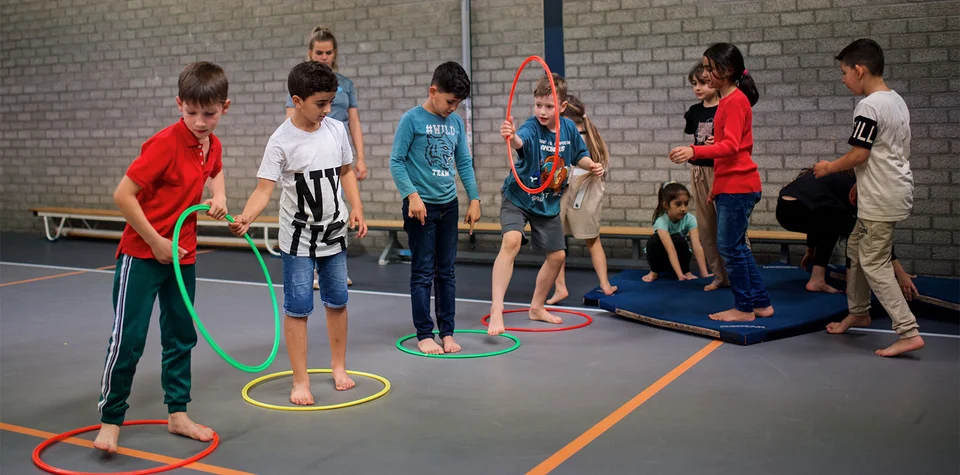 kinderen spelen met elkaar in een gymzaal met gekleurde hoepels
