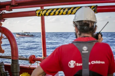 CH128955-A-Save-the-Children-team-member-looks-out-at-a-boat-crowded-with-refugees-and-migrants-in-the-Mediterranean-Sea.png