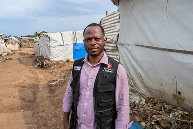 Gabriel staat in een vluchtelingenkamp in de DRC. Hij draagt een zwart Save the Children hesje.