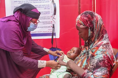 Een medewerker van Save the Children controleert of peuter Safana ondervoed is. Het meisje zit op schoot bij haar moeder.