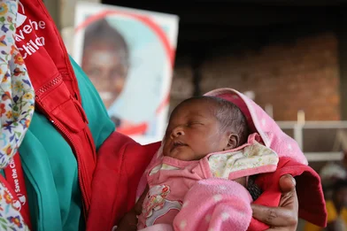 Medewerker van Save the Children houdt een pasgeboren baby vast bij een noodhulpkliniek