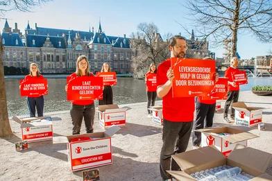 Medewerkers van Save the Children staan met borden voor de hofvijver in Den Haag