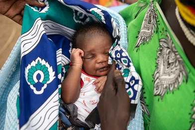 Een baby slaapt in de armen van zijn moeder. Hij is gewikkeld in kleurrijke doeken
