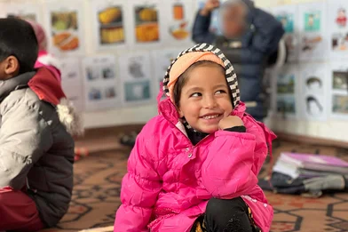 Kind 4 jaar in knalroze witerjaszit op de grond in een klas voor dove kinderen in Kabul