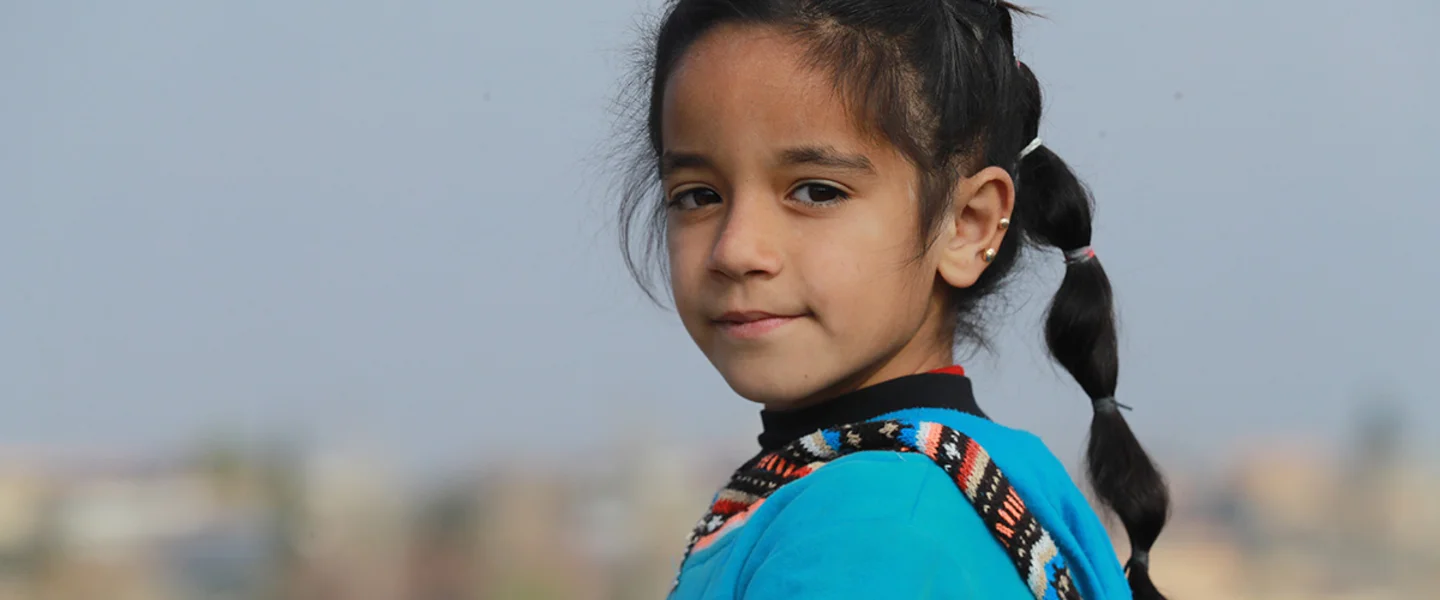 De achtjarige Amal kijkt in de camera, terwijl ze in een vluchtelingenkamp in Syrië staat