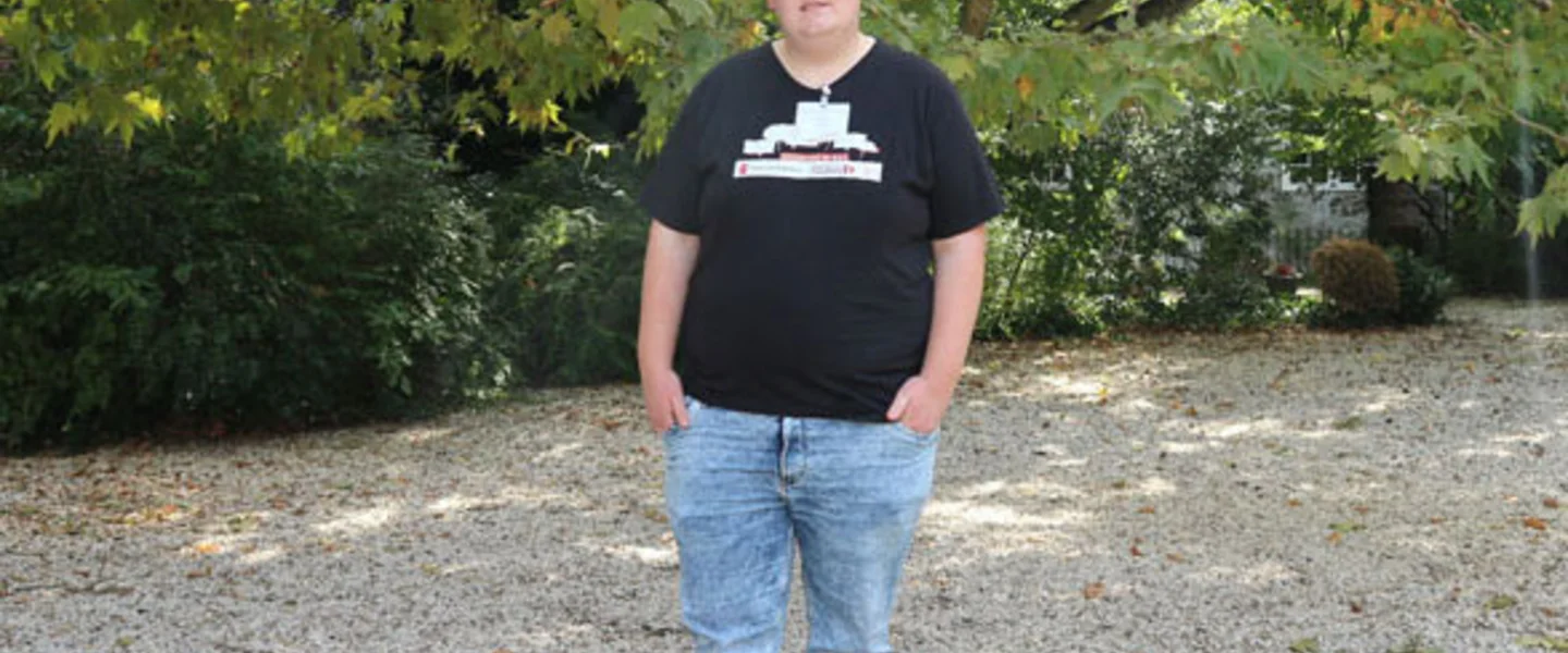 Portret van jongerenambassadeur Melvin ten voeten uit. Hij draagt een zwart T-shirt en een spijkerbroek.