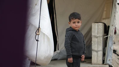 Jongetje staat voor een tent. Hij kijkt recht de camera in.