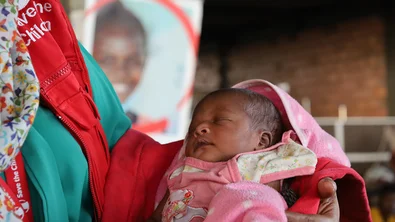 Medewerker van Save the Children houdt een pasgeboren baby vast bij een noodhulpkliniek