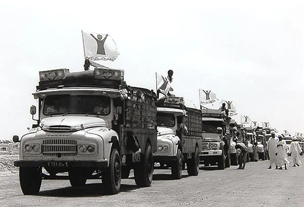 een kolonne van trucks met wapperende vlaggen van Save The Children rijden over een weg