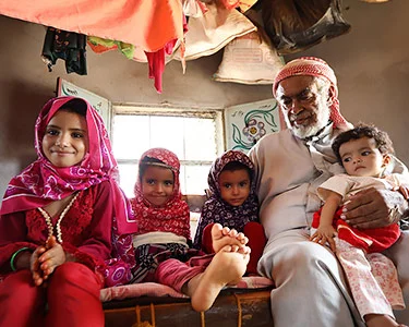 Familie in Jemen, drie kleine meisjes en een jongetje met vader in hun huis voor het raam. Ze kijken blij.