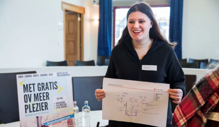 Speaking Minds - Leerling houdt een papier vast met daarop een presentatie, ze kijkt blij.