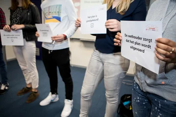 Jongeren houden een vel met tekst voor zich tijdens de opdracht ‘hoe maak je beleid’