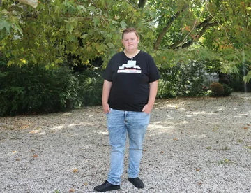 Portret van jongerenambassadeur Melvin ten voeten uit. Hij draagt een zwart T-shirt en een spijkerbroek.